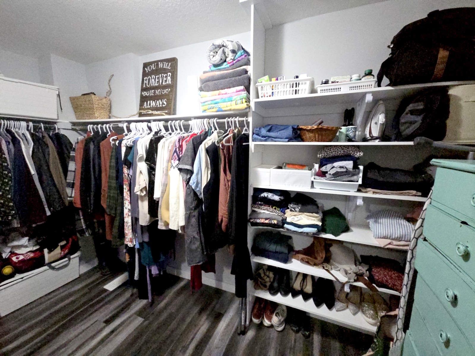 Walk-in closet with clothing organized by category on open shelving, folded linens stacked above, and shoes lined up below.